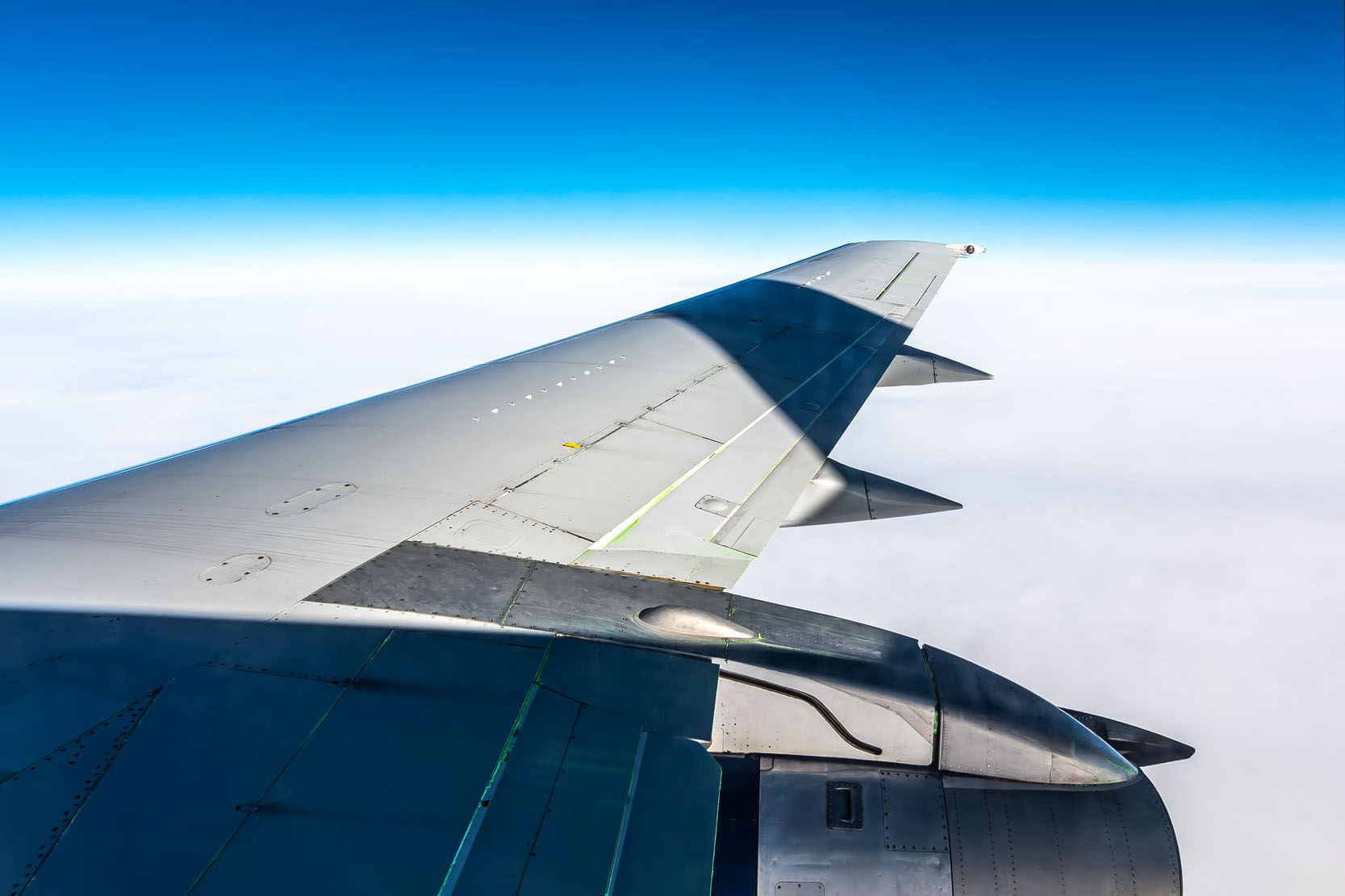 Vue d'un aile d'avion en vol, avec un ciel bleu clair et des nuages blancs en dessous, soulignant l'altitude.