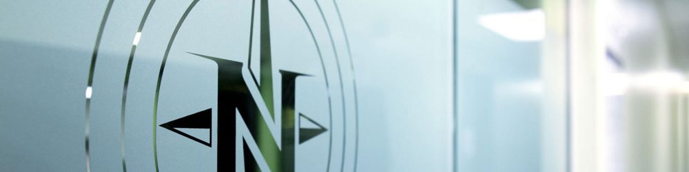 Logo stylisé avec une lettre N et des flèches directionnelles sur une surface en verre, évoquant un environnement moderne et professionnel.