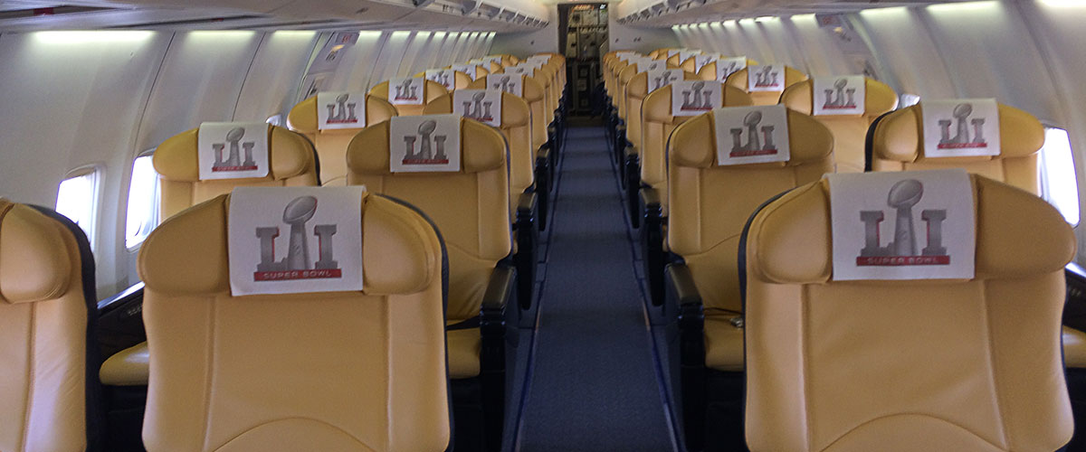 Interior of an airplane featuring rows of yellow seats, each with a Super Bowl-themed headrest cover.