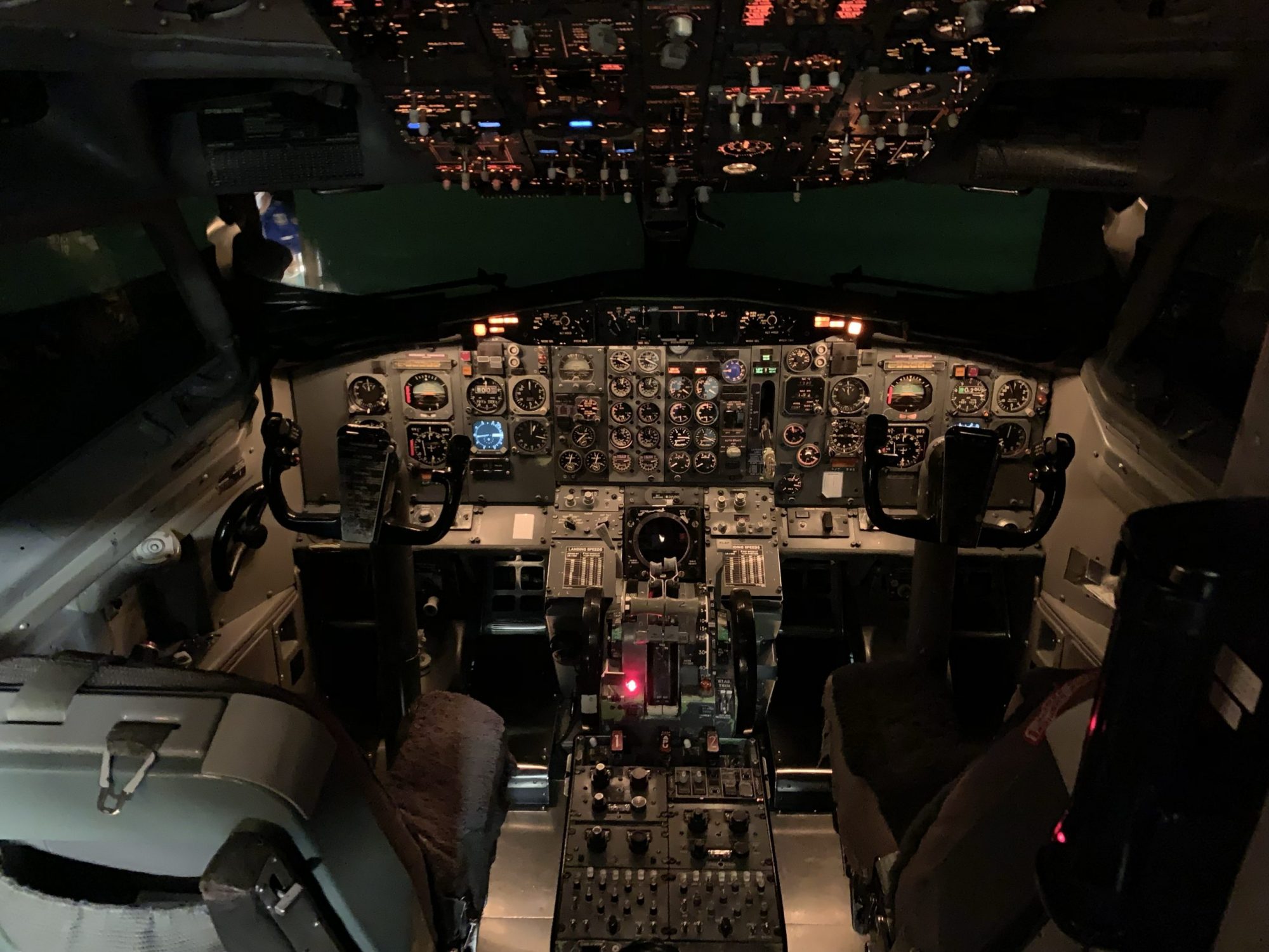 Cockpit of a commercial aircraft featuring various controls, gauges, and illuminated panels, with two pilot seats visible.