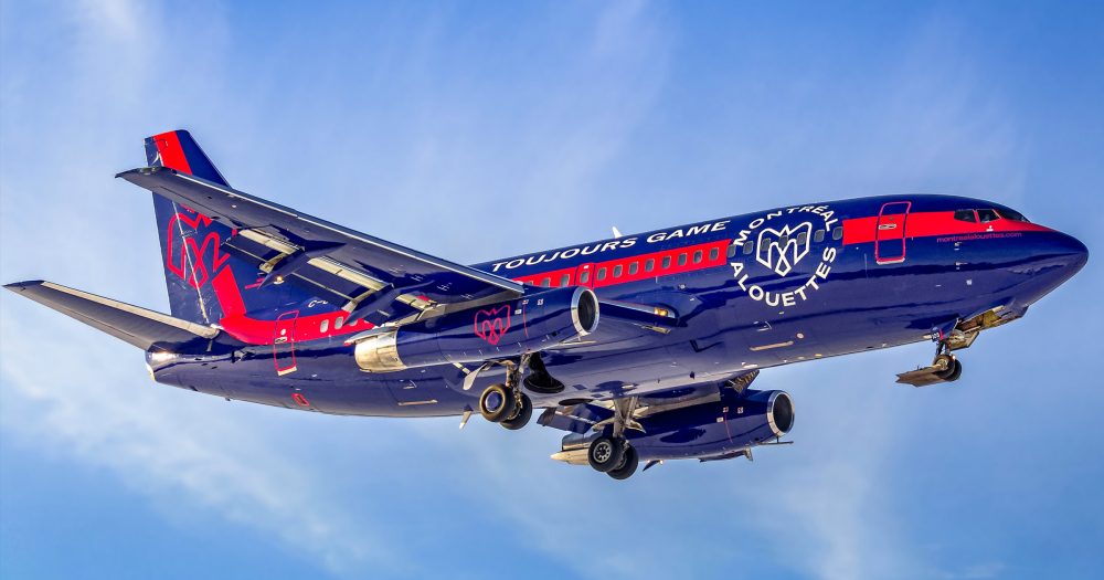 A blue and red airplane with "Toujours Game" and "Montreal" branding descends against a clear sky.
