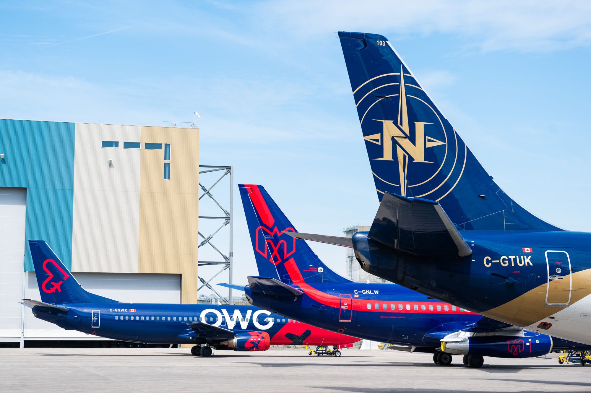 Deux avions de ligne stationnés sur le tarmac, l'un avec une livrée rouge et bleue et l'autre en bleu foncé avec un logo doré.