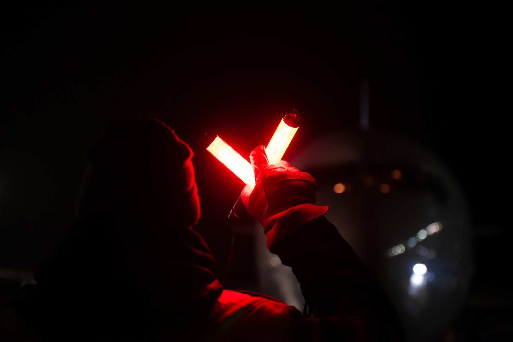 Un agent de sécurité utilise des bâtons lumineux rouges pour diriger un avion sur le tarmac, dans un environnement nocturne.