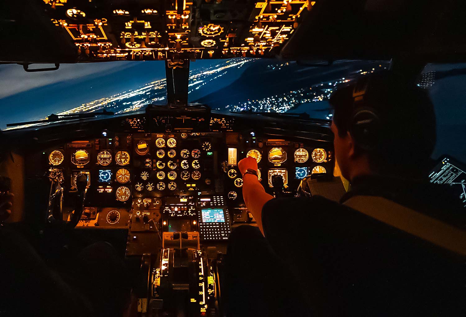 Un pilote manœuvre un avion de nuit, entouré de tableaux de bord éclairés et d'instruments de navigation, avec des lumières de la ville en arrière-plan.