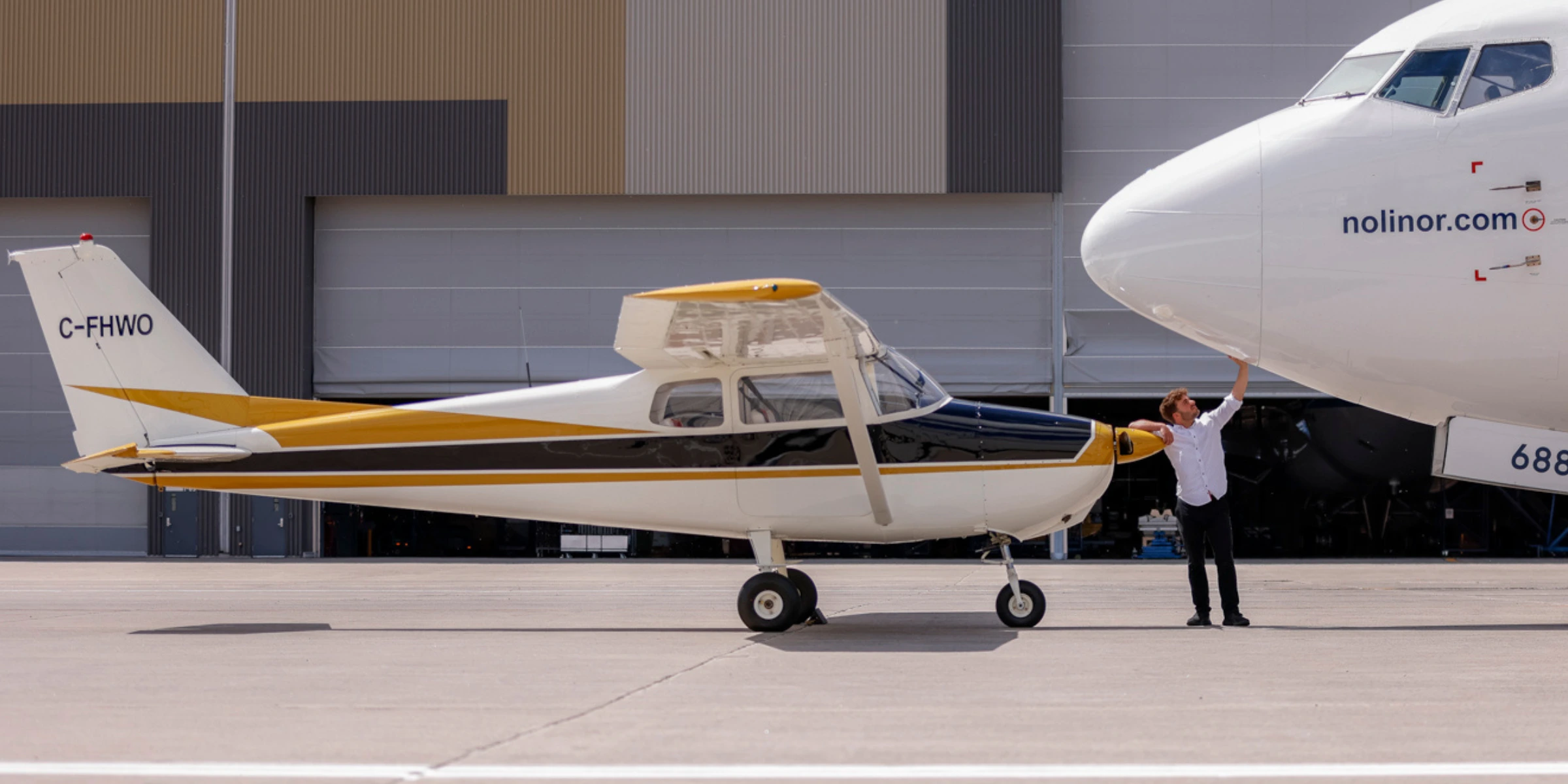 A pilot inspects a small yellow and black aircraft next to a larger white airplane on a tarmac.