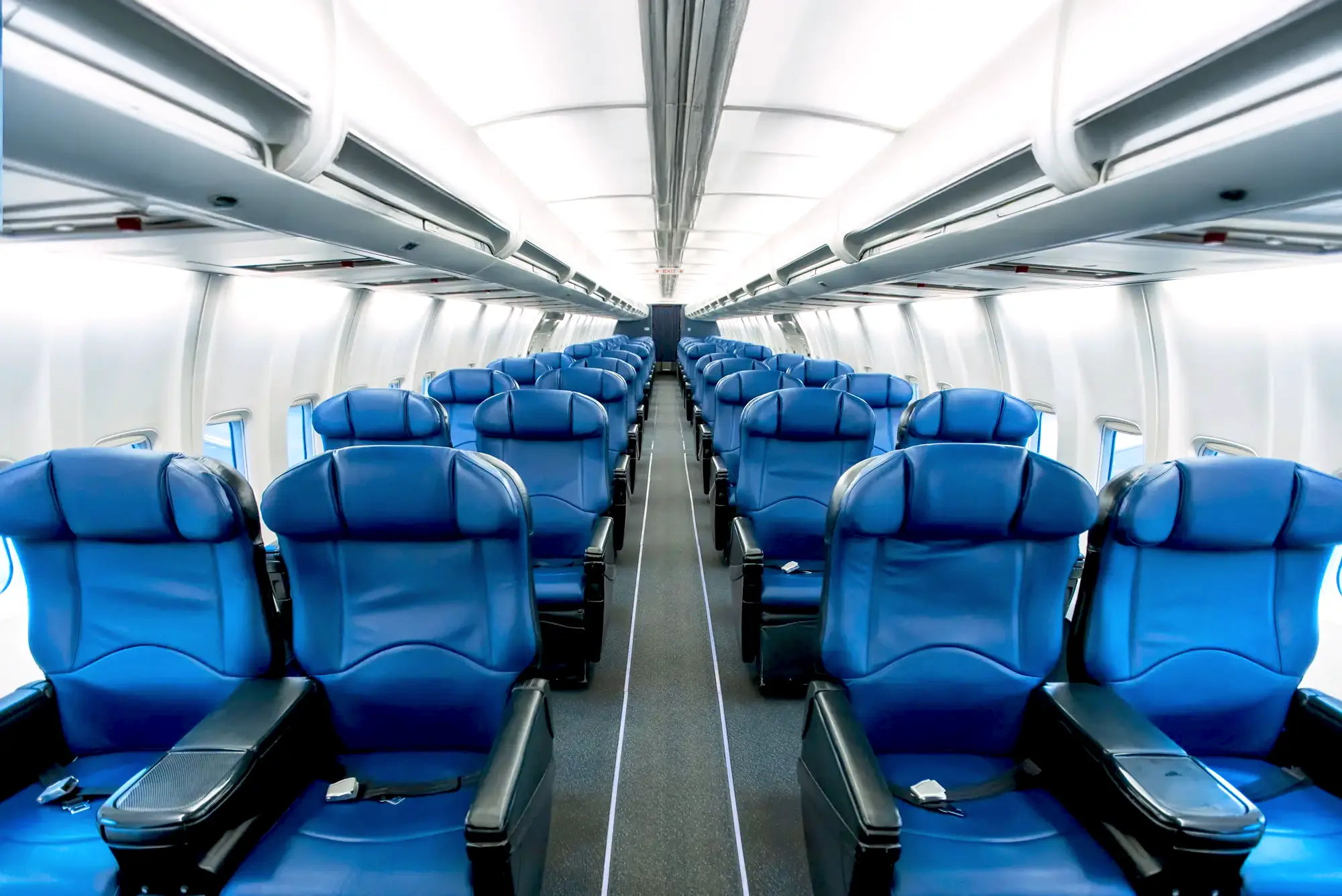 Cabine d'avion avec rangées de sièges bleus vides, éclairage clair et allée centrale dégagée, ambiance moderne et spacieuse.