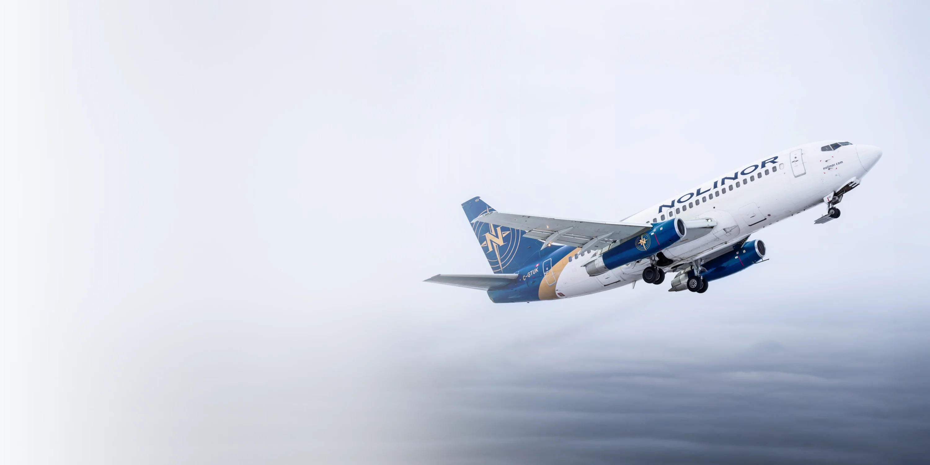 A Nolinor airplane takes off against a cloudy sky, ascending with its nose pointed upward.