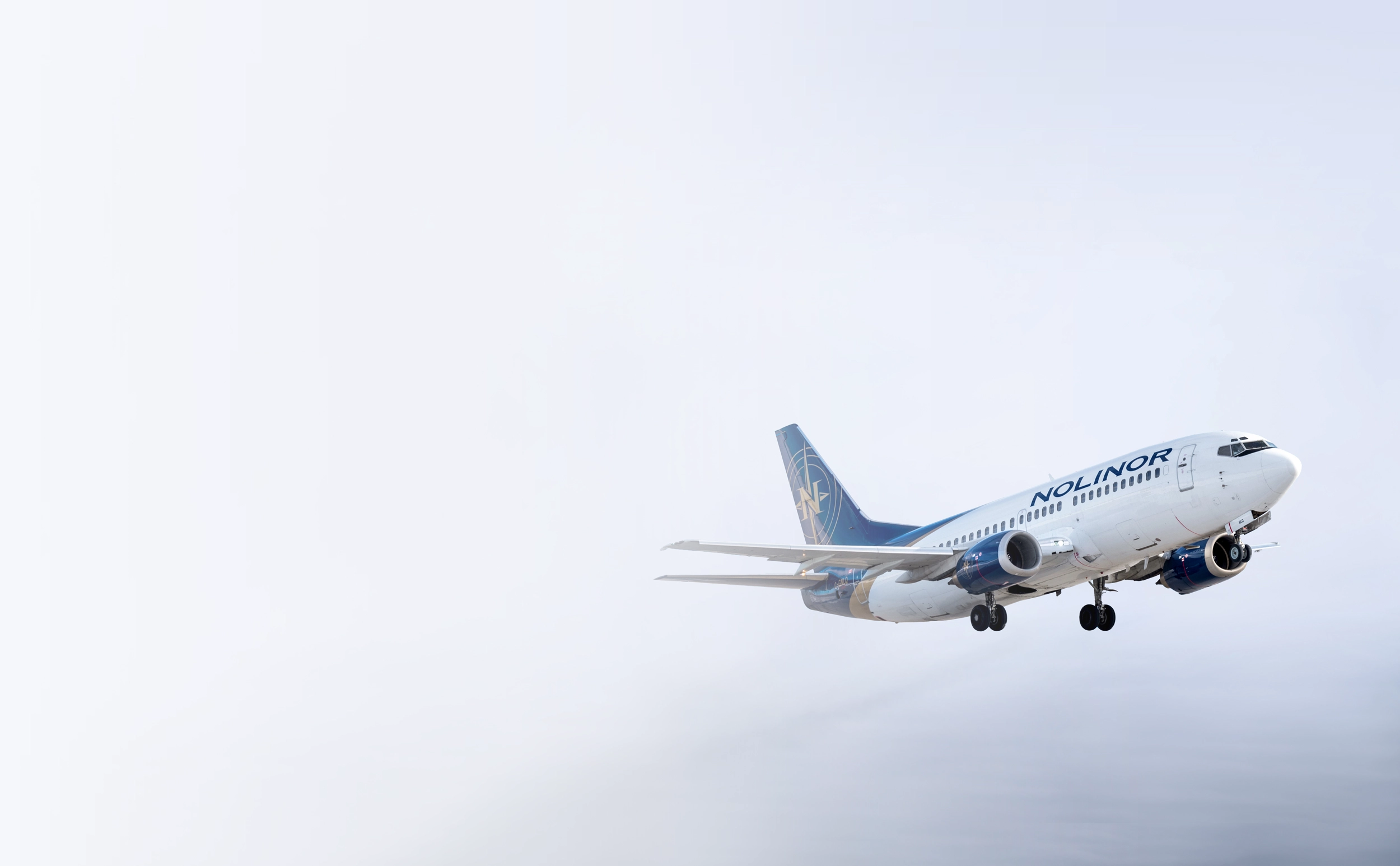 Un avion de la compagnie Nolinor en phase d'atterrissage, avec un ciel nuageux en arrière-plan.