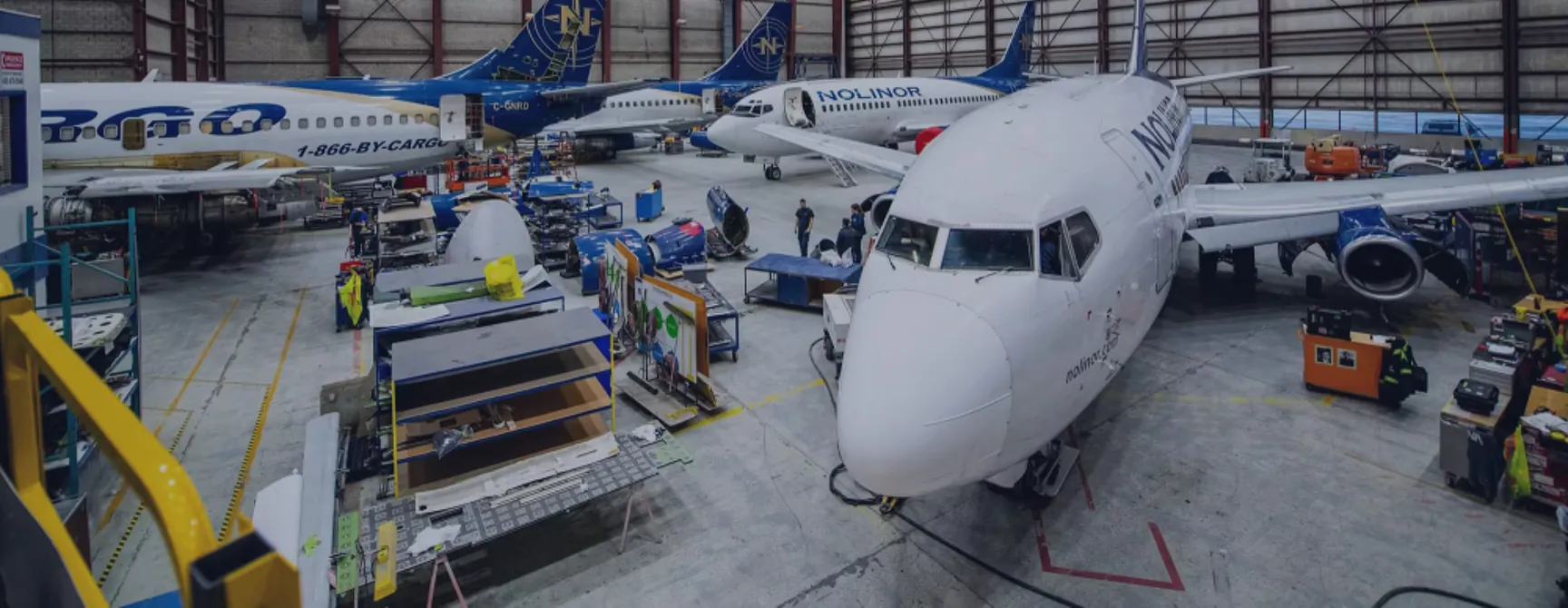 Un hangar d'entretien aéronautique avec plusieurs avions en cours de réparation. Des techniciens travaillent autour des avions et des équipements.