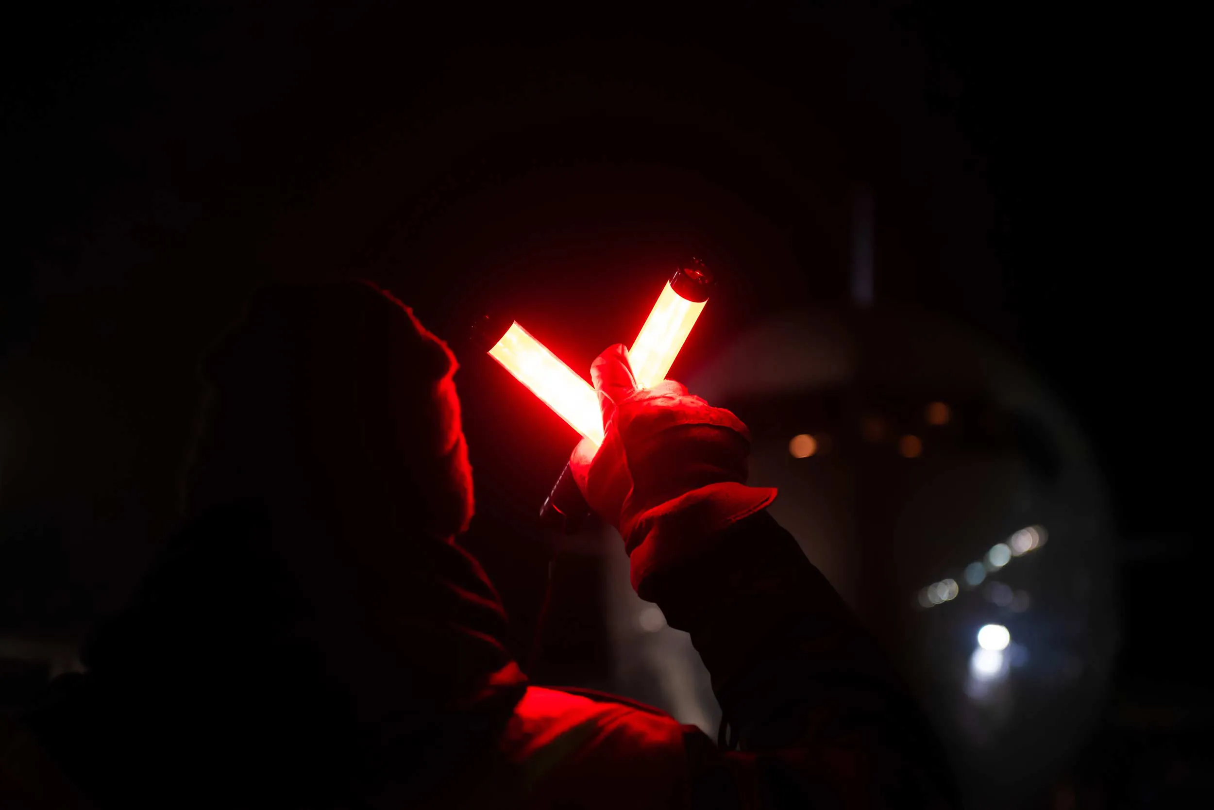 Un agent de sécurité utilise des bâtons lumineux rouges pour diriger un avion sur le tarmac, dans un environnement nocturne.