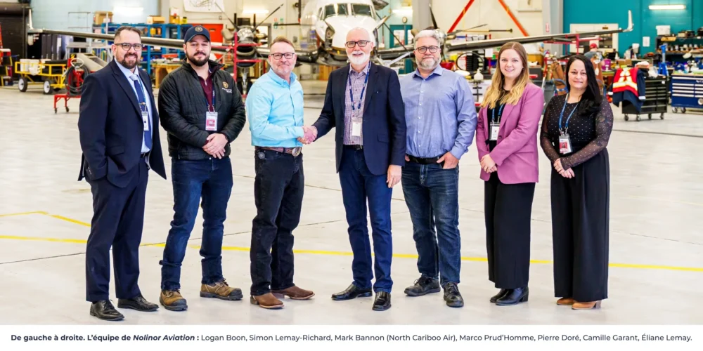 L'équipe de Nolinor Aviation se tient dans un hangar, souriante, après une remise de prix. Des avions sont visibles en arrière-plan.