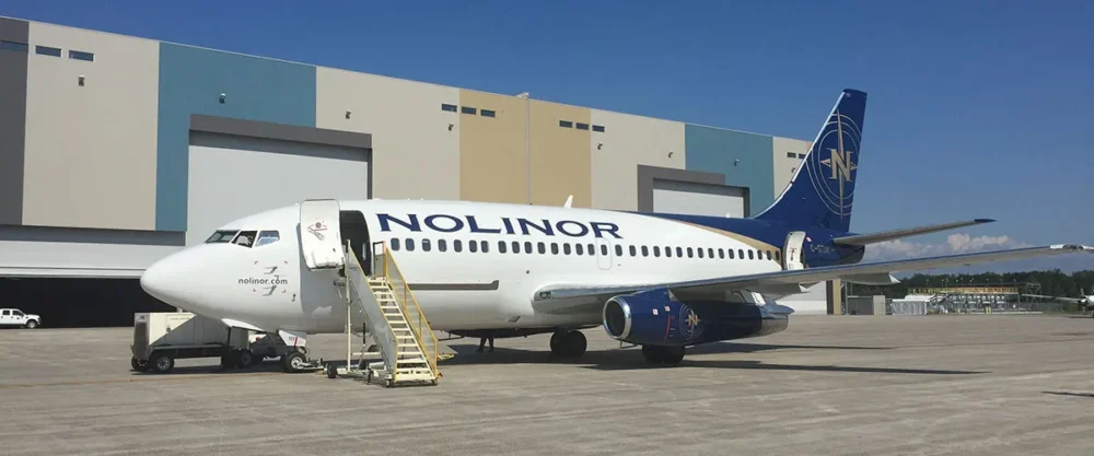 A Nolinor Aviation aircraft parked at a hangar, with stairs leading up to the entrance, showcasing its blue and white livery.