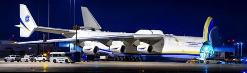 Un avion cargo imposant est stationné sur le tarmac nocturne, avec des véhicules de service à proximité et une cargaison en cours de chargement.