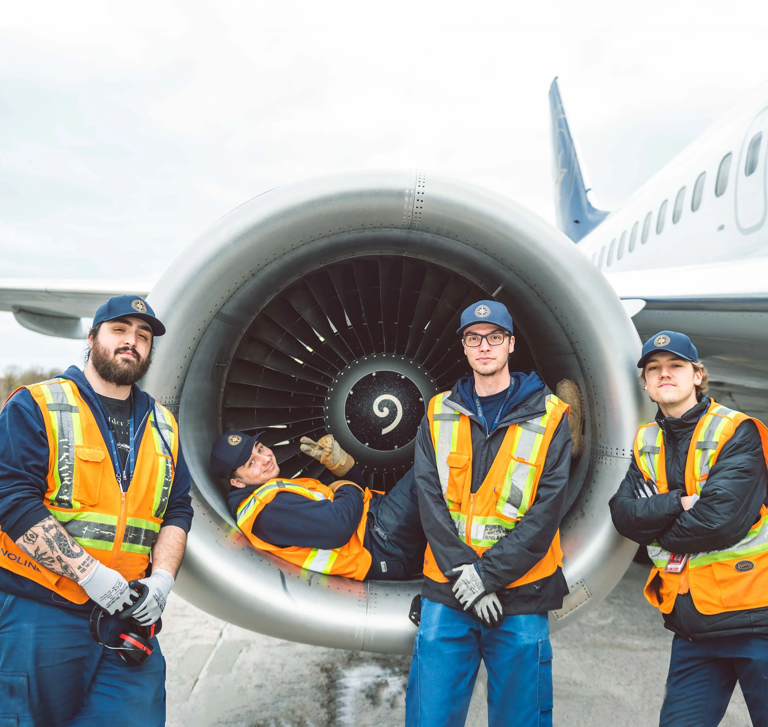 Quatre techniciens d'aéroport posent près d'un moteur d'avion, vêtus de gilets de sécurité orange et de casquettes.
