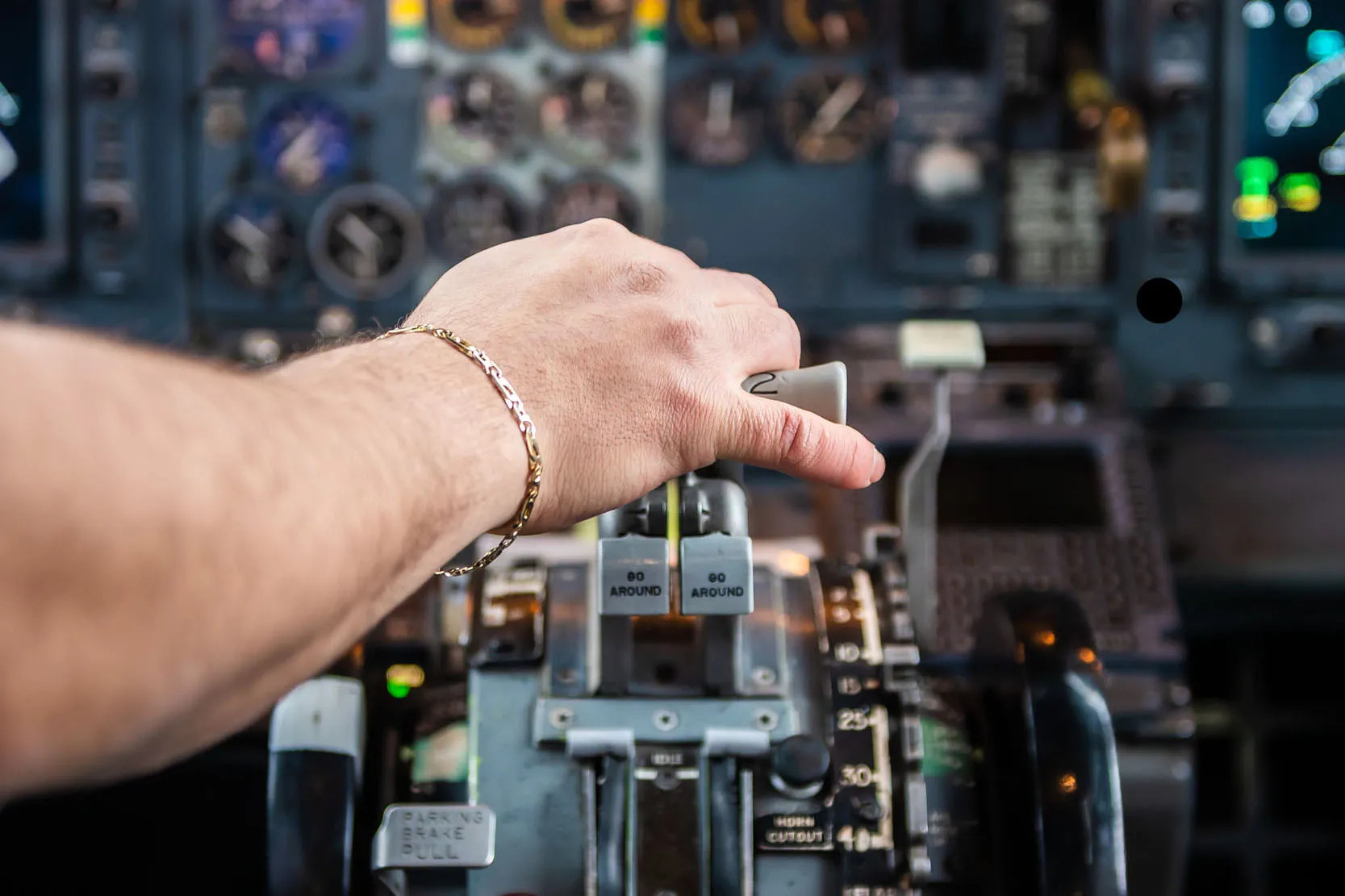 Un pilote ajuste les manettes de contrôle dans le cockpit d'un avion, avec des instruments et écrans visibles en arrière-plan.