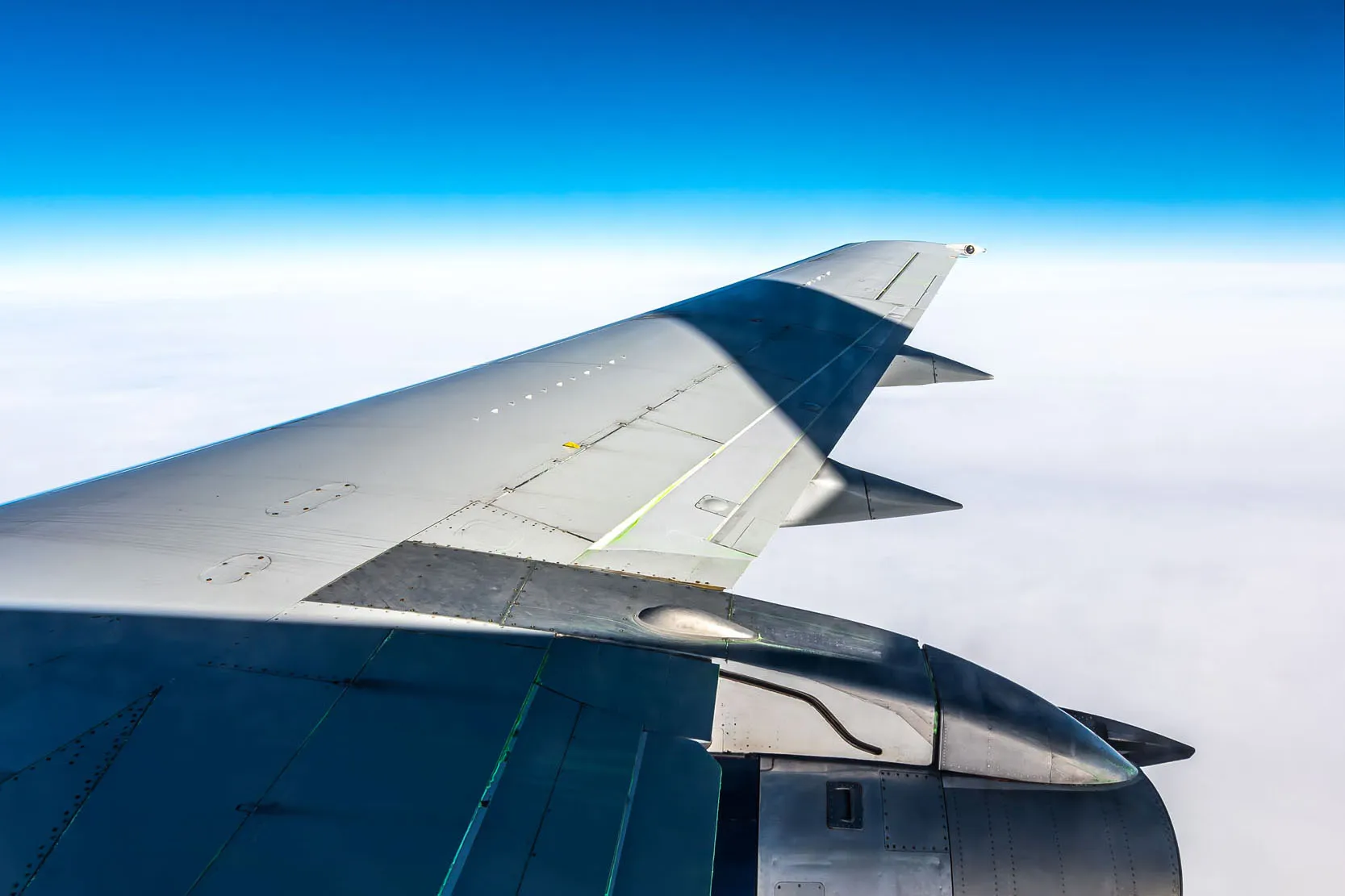 Vue d'un aile d'avion en vol, avec un ciel bleu clair et des nuages blancs en dessous, soulignant l'altitude.