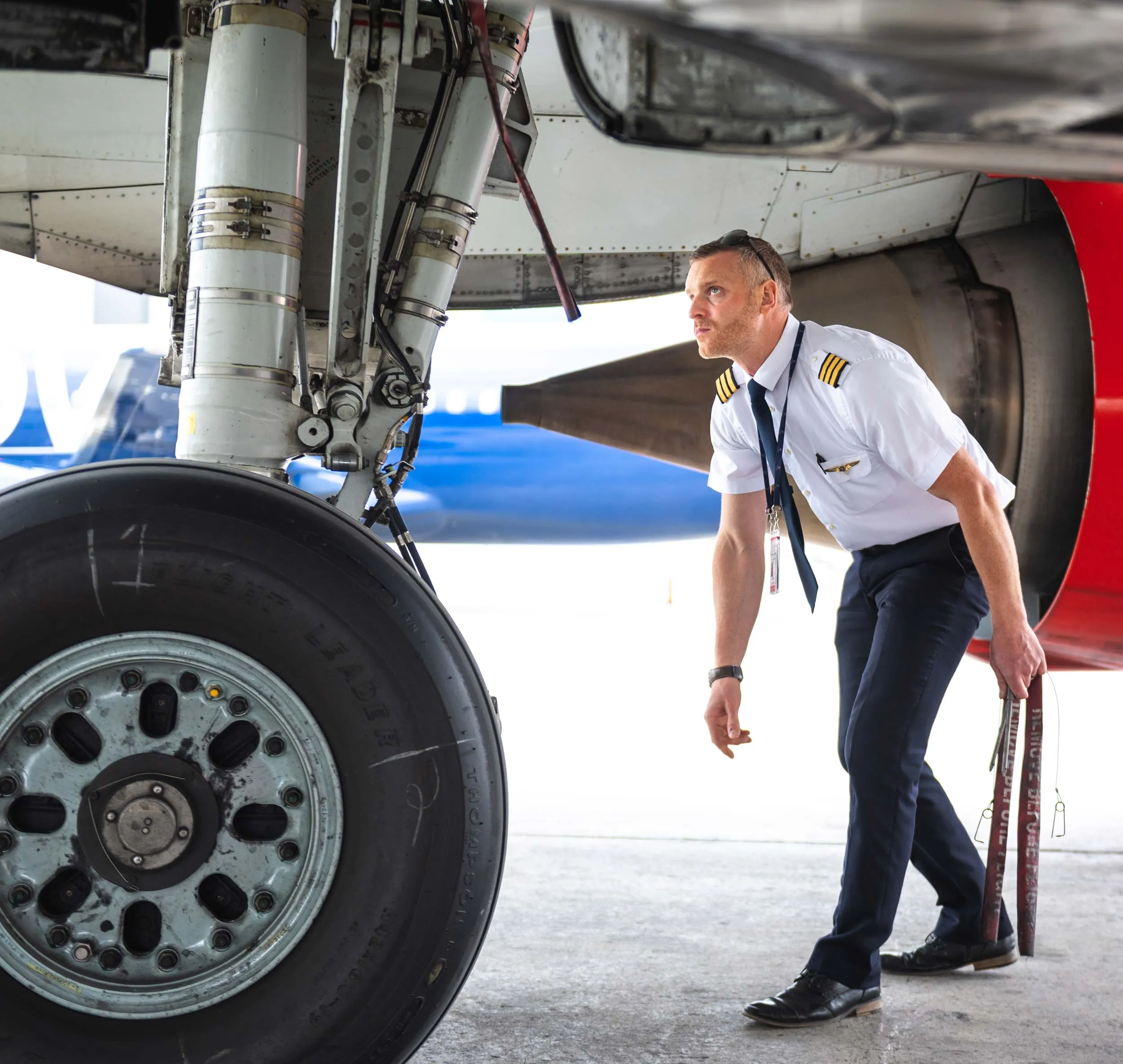 Un pilote inspecte le train d'atterrissage d'un avion, concentré sur les détails techniques avant le vol. L'environnement est un aéroport.